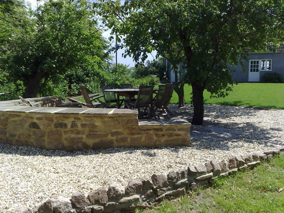 A raised natural stone seating area with gravel, a stone-edged border, lawn and an apple tree