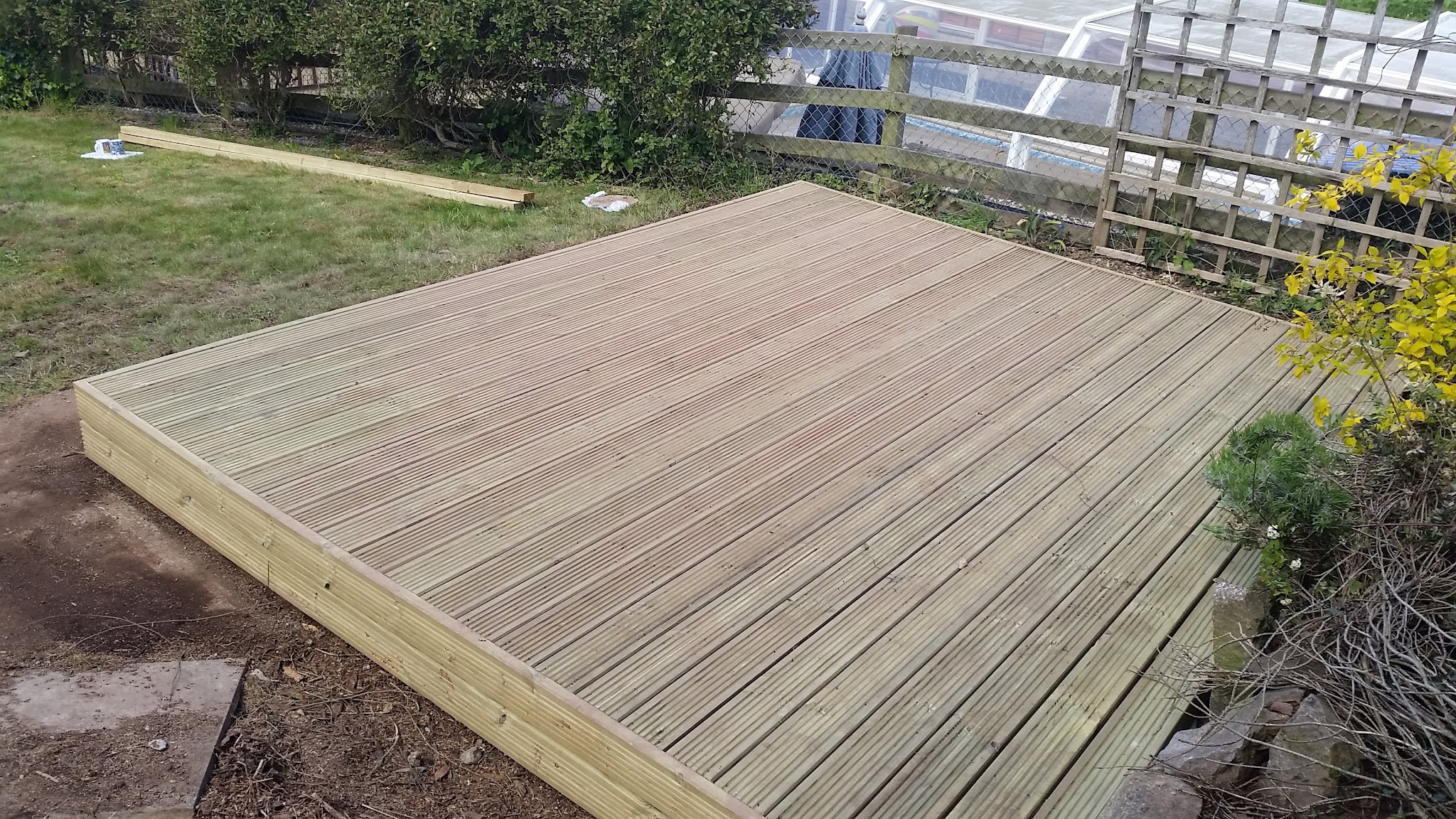 A new softwood deck laid on its frame beside a lattice-topped fence