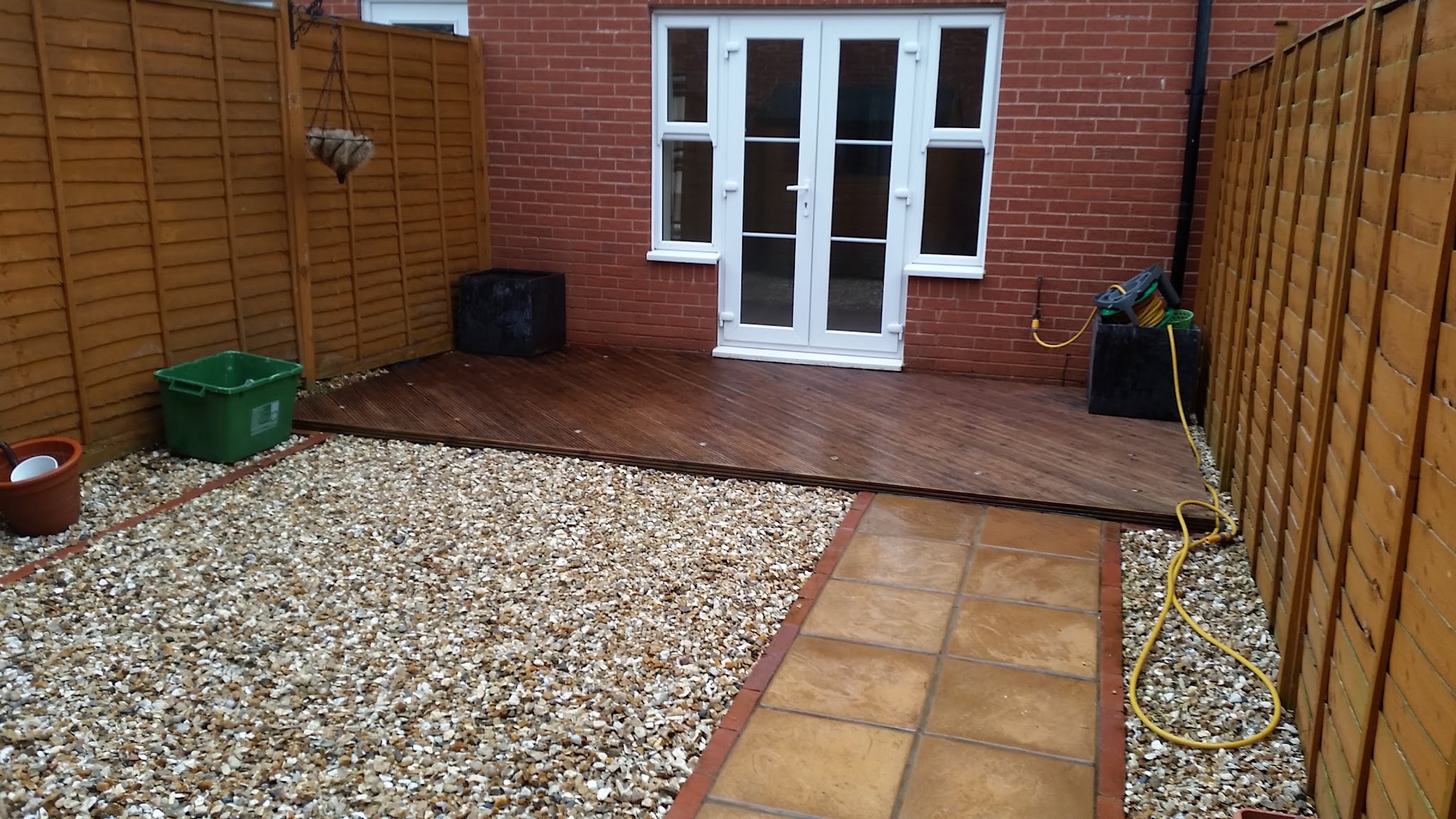 A small back garden with a dark timber deck by French doors, gravel and a flag path