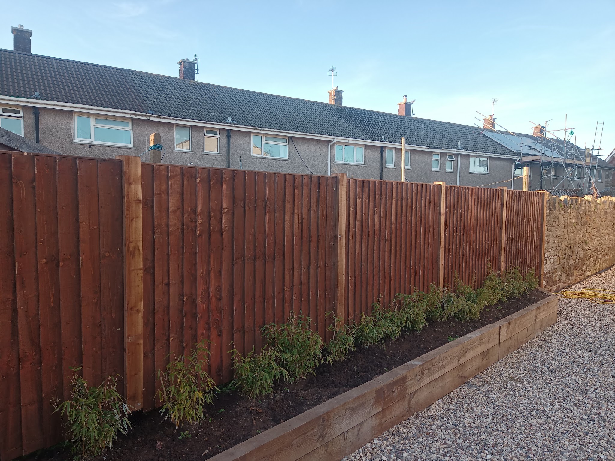 A long run of new closeboard fencing with a sleeper raised bed and gravel