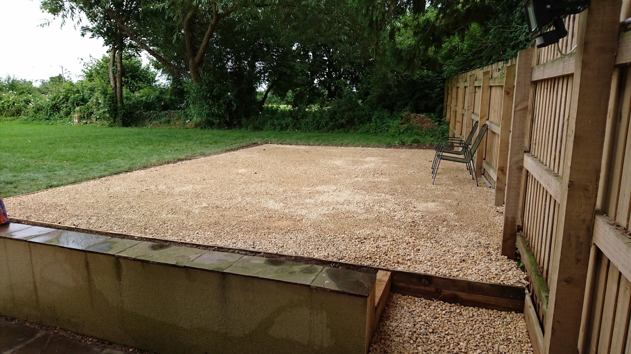 A levelled gravel area with a timber sleeper retaining edge beside a fence